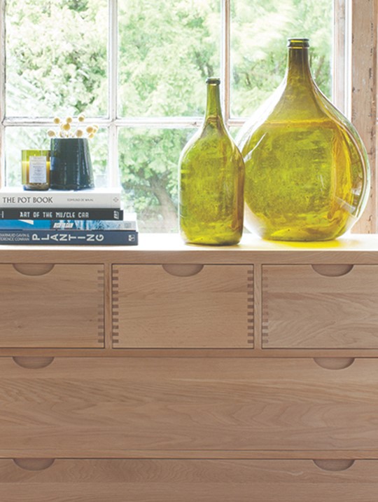 Ercol Bosco Bedroom Oak 5 Drawer Chest Displaying Two Large Vases In Front of a Big Window