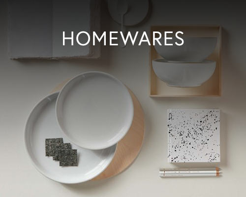 Flat lay of minimalist white homeware items including plates, bowls, pencils, and a speckled notebook on a neutral background.