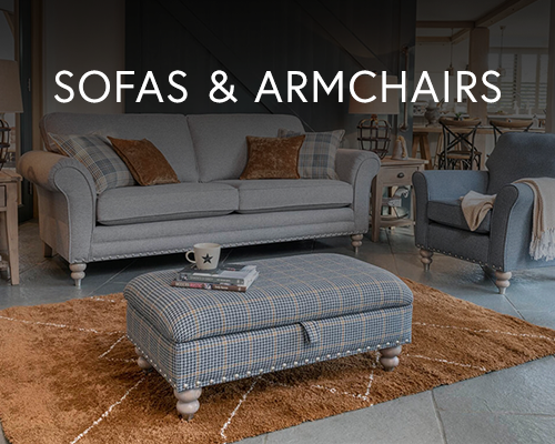 Cosy living space featuring a grey sofa and armchair with tartan footstool and brown cushions on a soft rug.