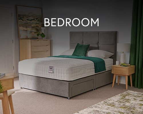 Contemporary bedroom with a grey upholstered bed, white mattress, green throw, and matching wooden furniture.
